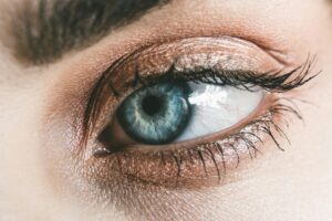 Primo piano di un occhio azzurro con dettagli nitidi dell’iride e ombretto dorato. L’immagine è utilizzata per illustrare la varietà cromatica dell’iride umana e introdurre il tema del colore degli occhi come tratto genetico e simbolico. Il contrasto tra la precisione scientifica e le credenze culturali evidenzia come la percezione dell’occhio vada oltre la biologia, toccando storia, mito e personalità.